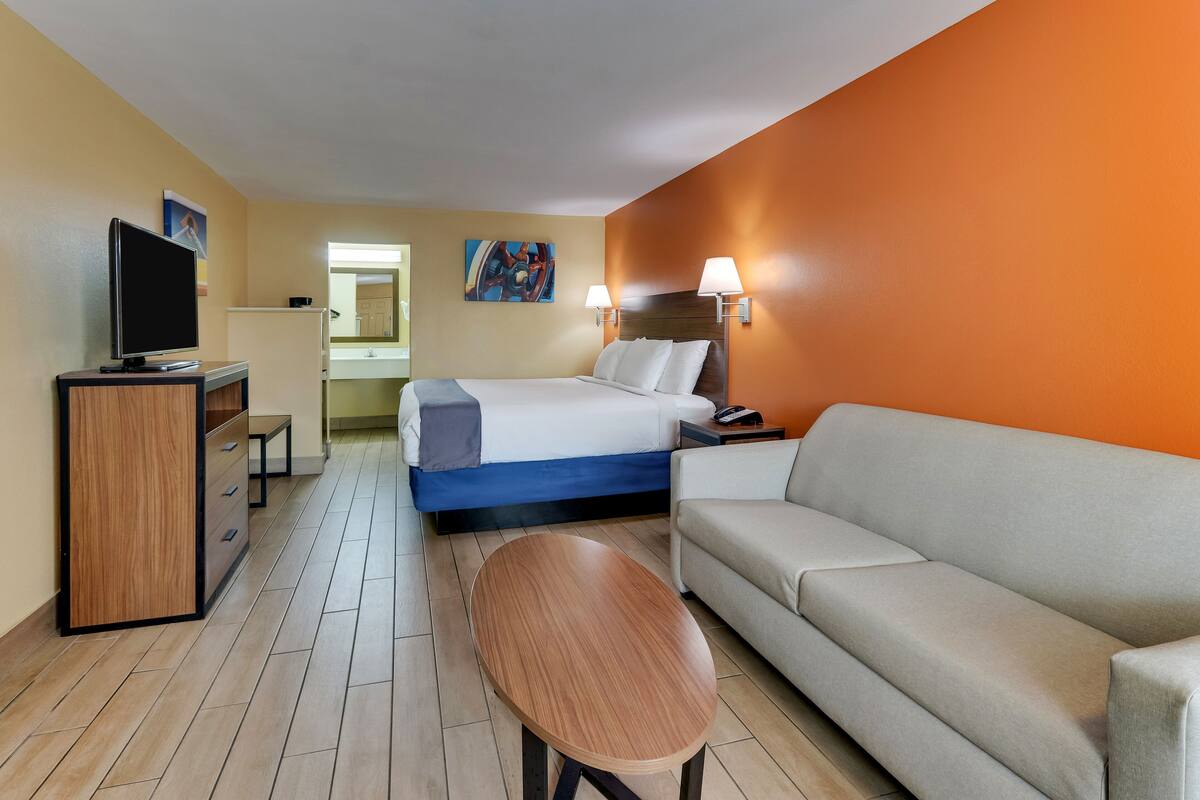 A hotel room with a bed, a sofa, a TV, a desk, and a lamp.