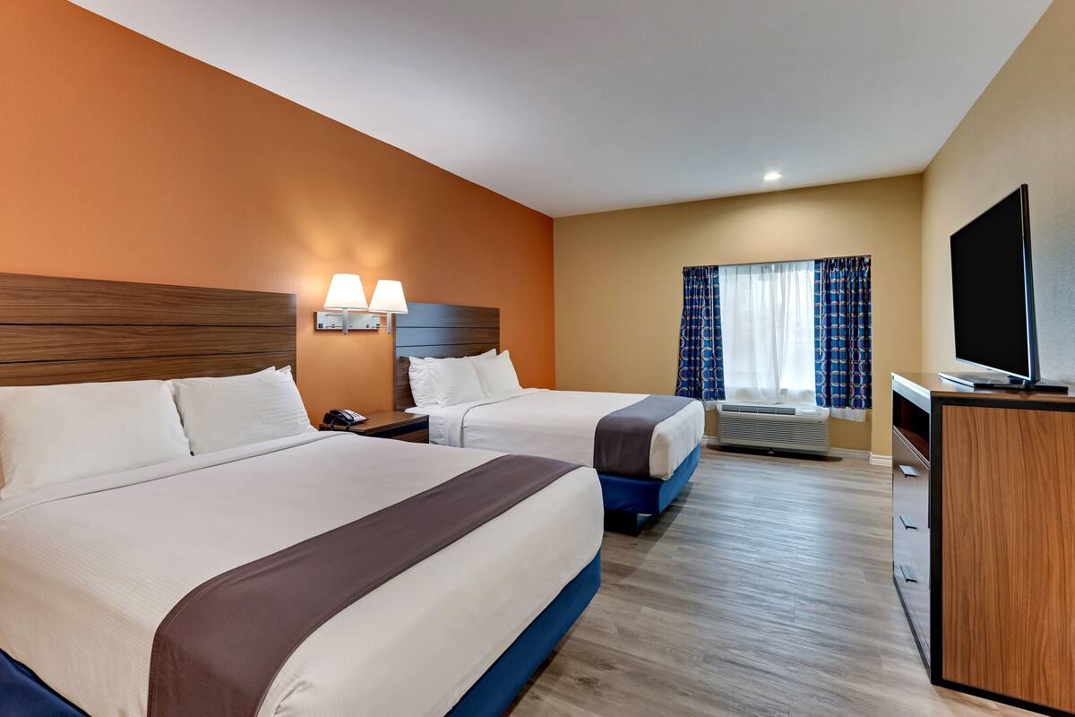 A hotel room with two beds, a desk, a television, and a window with curtains.