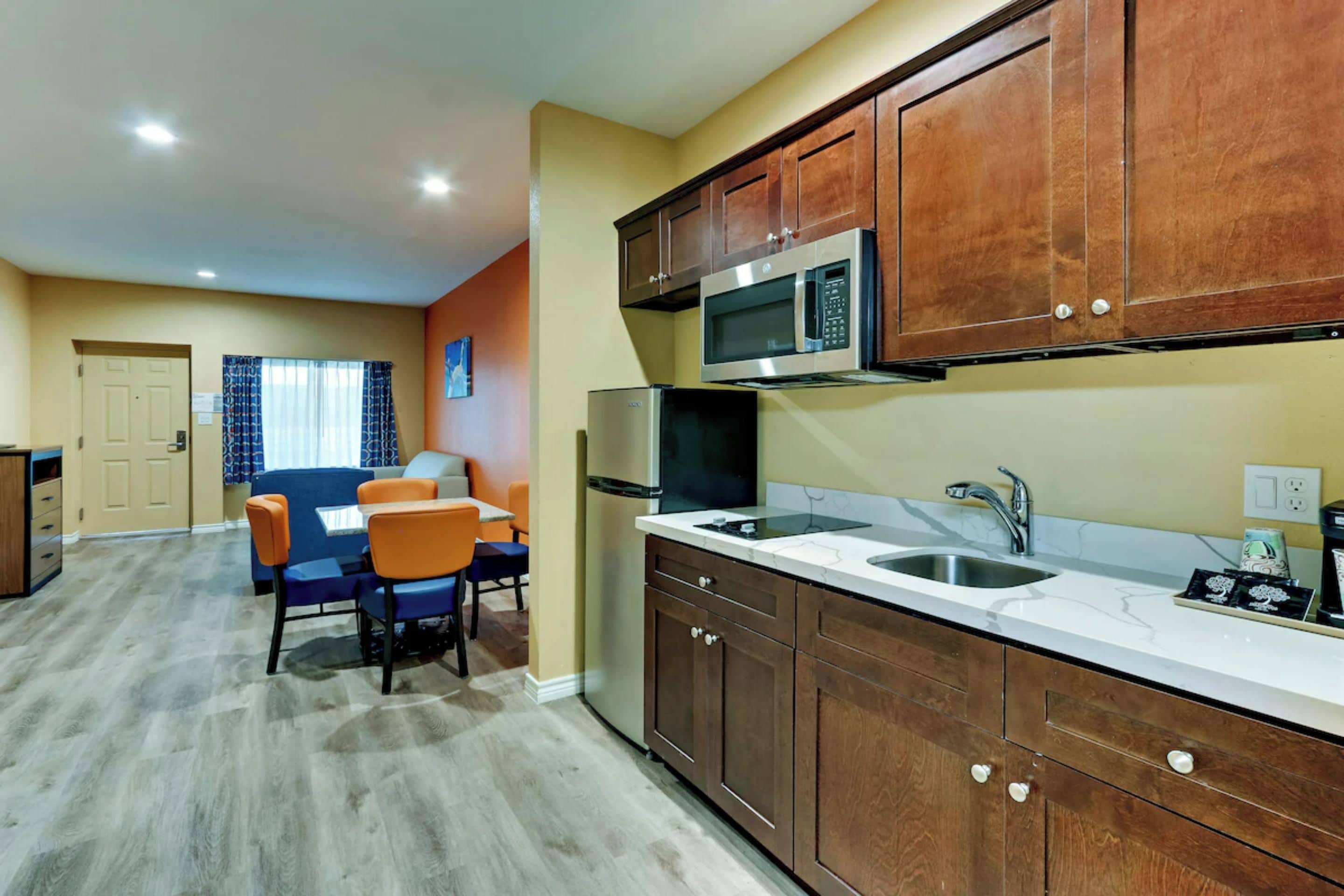 A compact kitchen with wooden cabinets, a microwave, a sink, and a dining area with chairs.