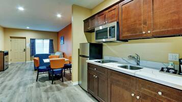 A compact kitchen with wooden cabinets, a microwave, a sink, and a dining area with chairs.