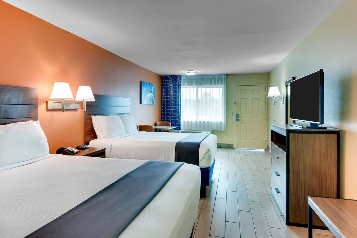 A hotel room with two beds, a TV, a desk, and a bathroom door.