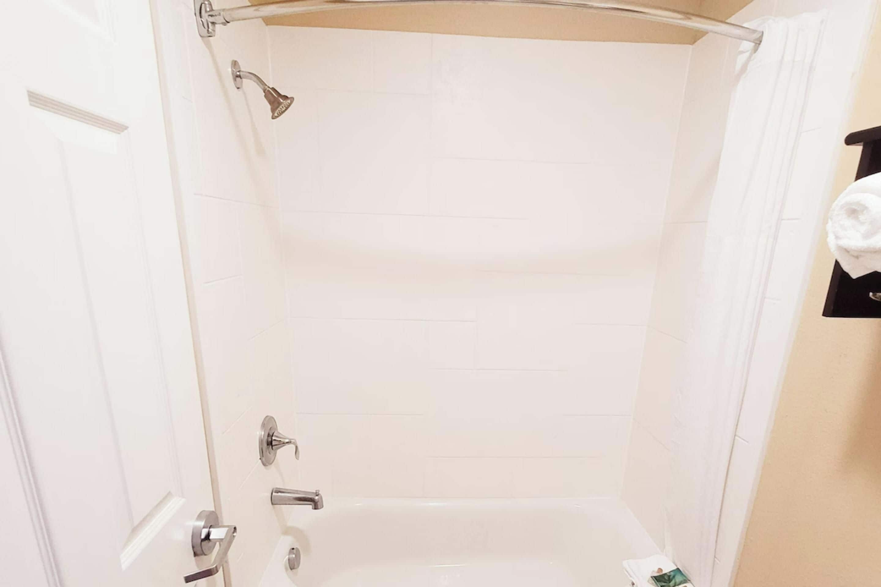 Aseo con ducha de azulejos blancos, cabezal de ducha, ducha de mano y toallero con una toalla enrollada.