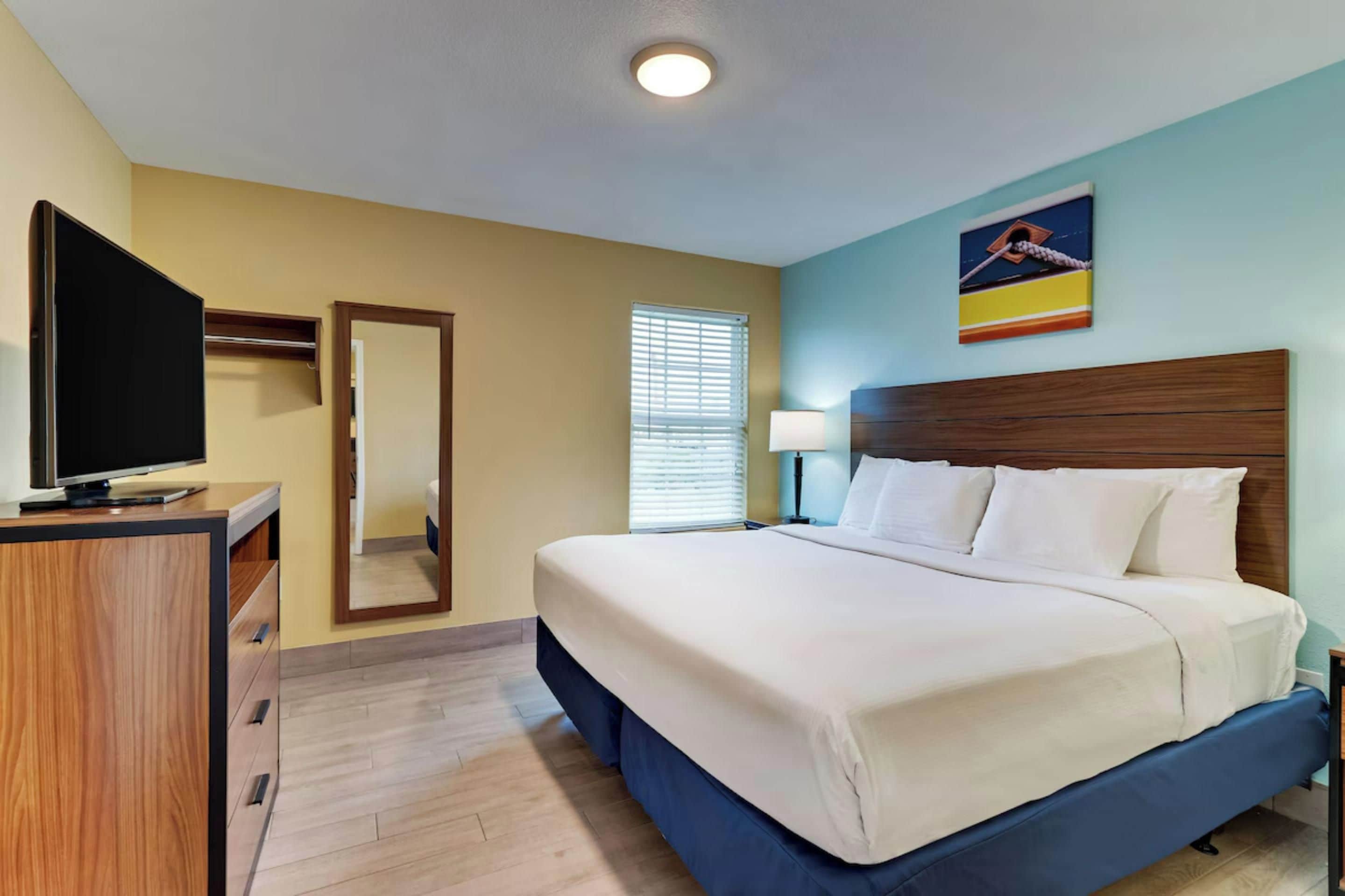 Una habitación de hotel con cama, televisor, escritorio y espejo.