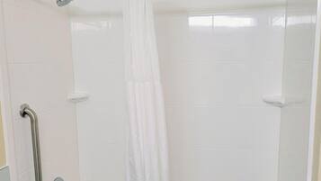 A shower area with white tiles, a showerhead, a handrail, and a curtain.