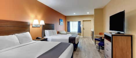 A hotel room with two beds, a desk, a television, and a bathroom visible in the background.