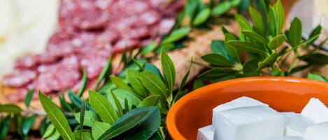 A bowl of white cubes, possibly cheese, surrounded by green leaves and a plate of sliced meats.