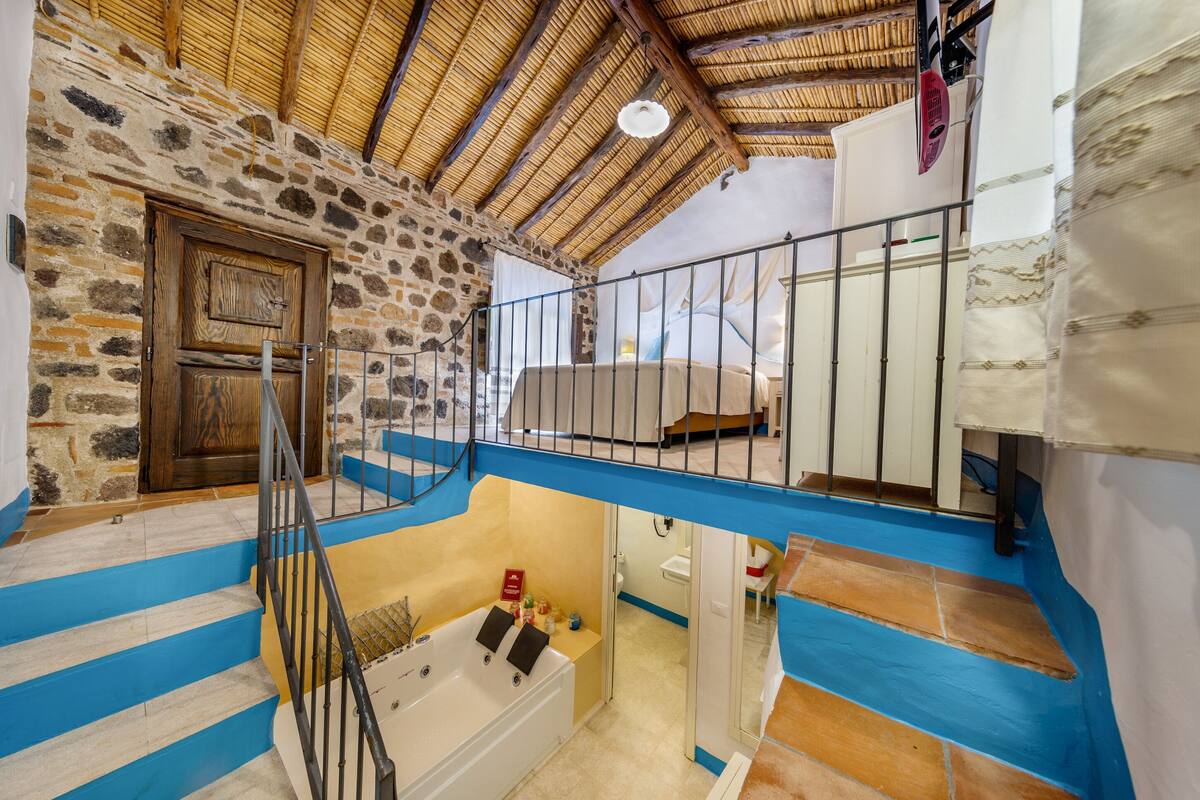 A stone-walled room with a wooden door, a bathtub, and a blue and white staircase.