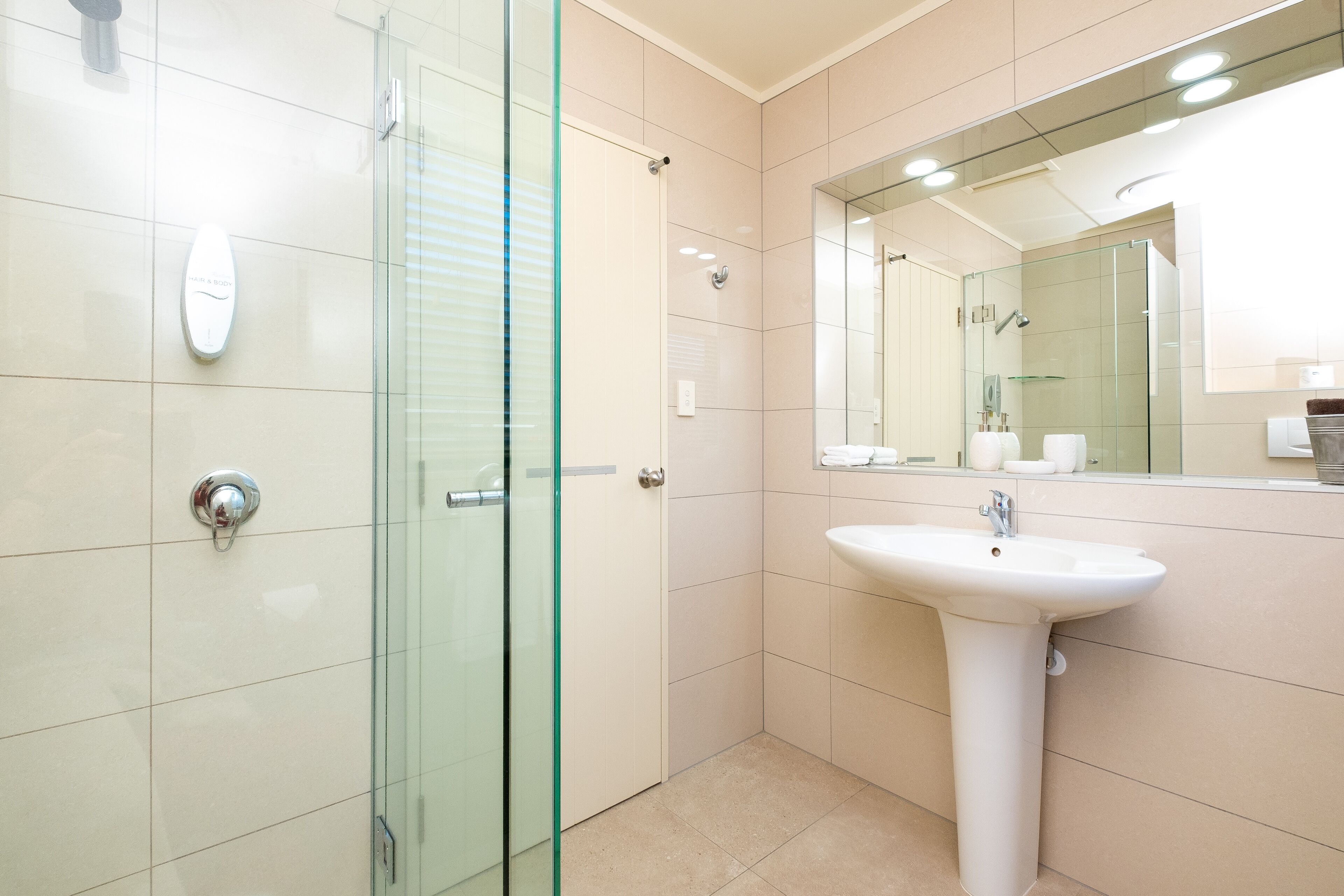 Une salle de bain moderne avec une douche à parois de verre, un lavabo blanc et un grand miroir.