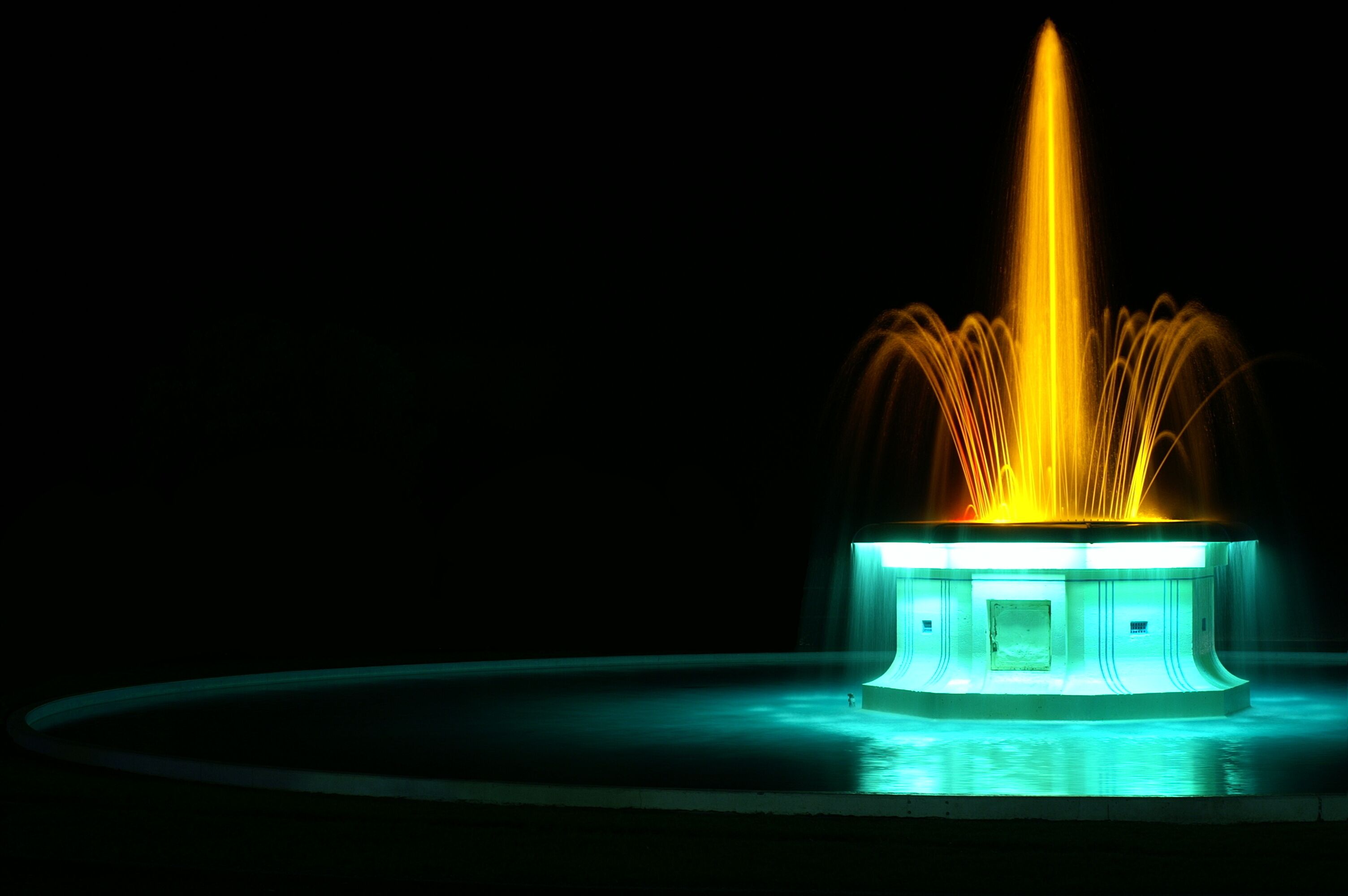 A fountain with a central jet of water, surrounded by a circular platform with a greenish glow.