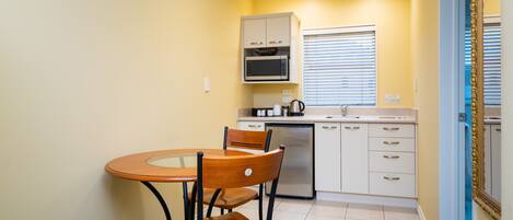A compact kitchen with a microwave, stove, and sink. There is a dining table with chairs and a window with blinds.