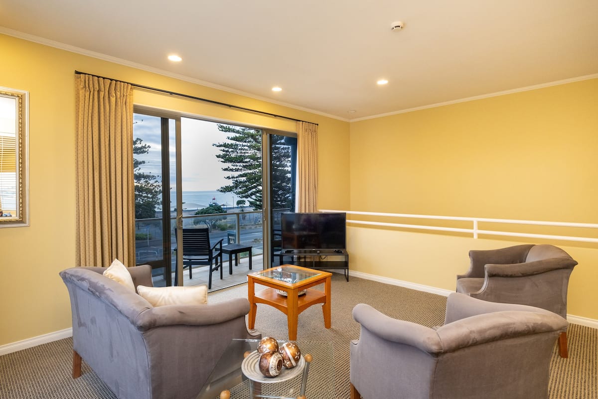 A living room with two sofas, a coffee table, a TV, and a large window with curtains.