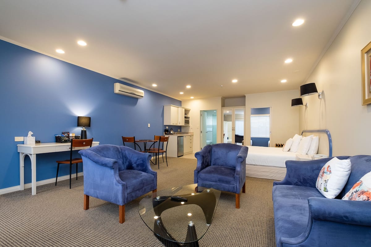 A hotel room with a blue wall, a bed, a sofa, a desk, and a kitchenette.