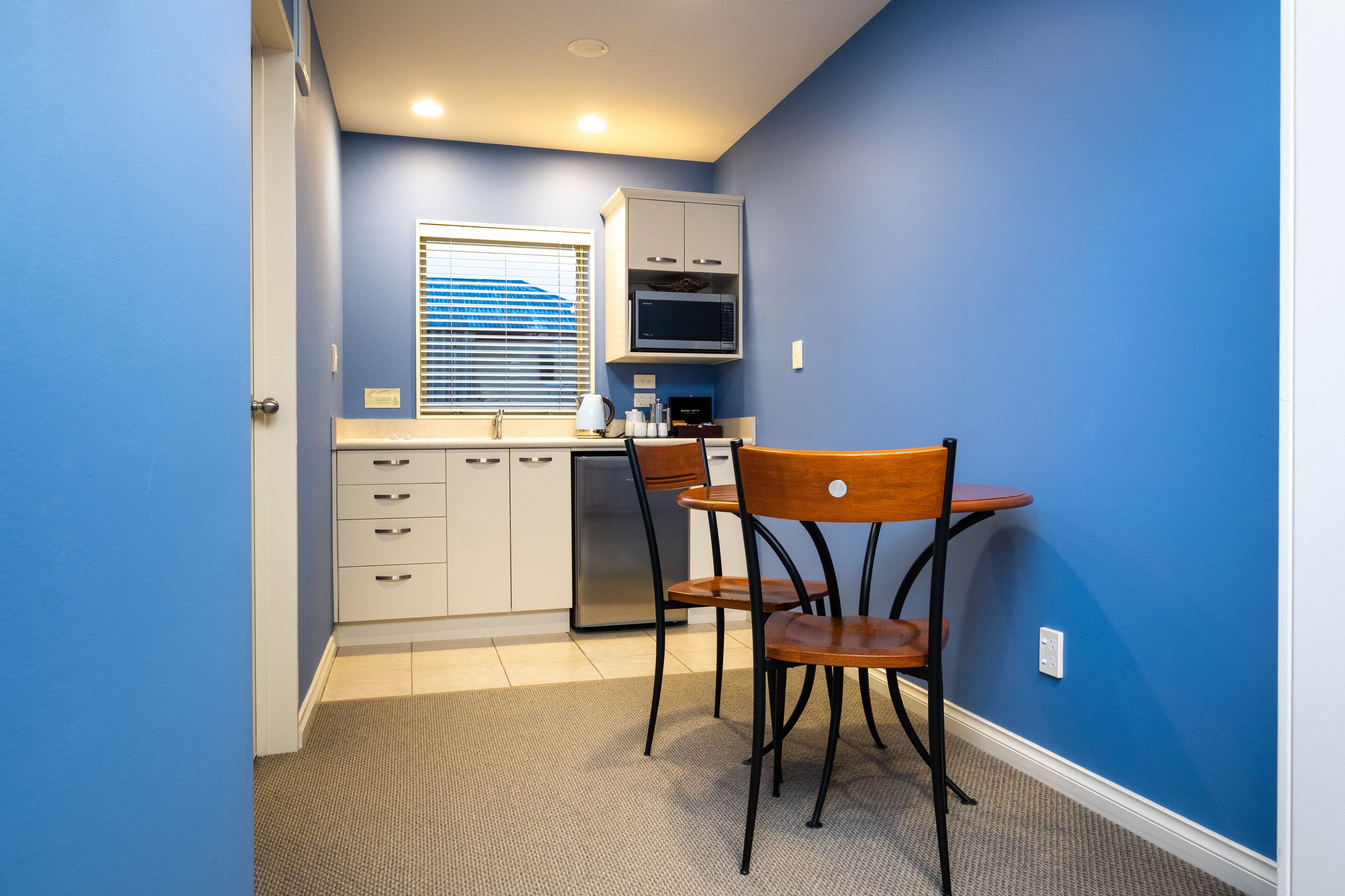 Una cocina compacta con microondas, refrigerador y un pequeño comedor con una silla y mesa.