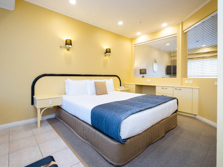A hotel room with a bed, bedside tables, a mirror, and a window with blinds.