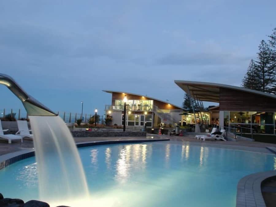 A swimming pool with a waterfall feature, lounge chairs, and a modern building with large windows.