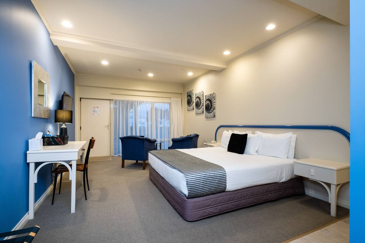 A hotel room with a bed, desk, chair, and a small table.