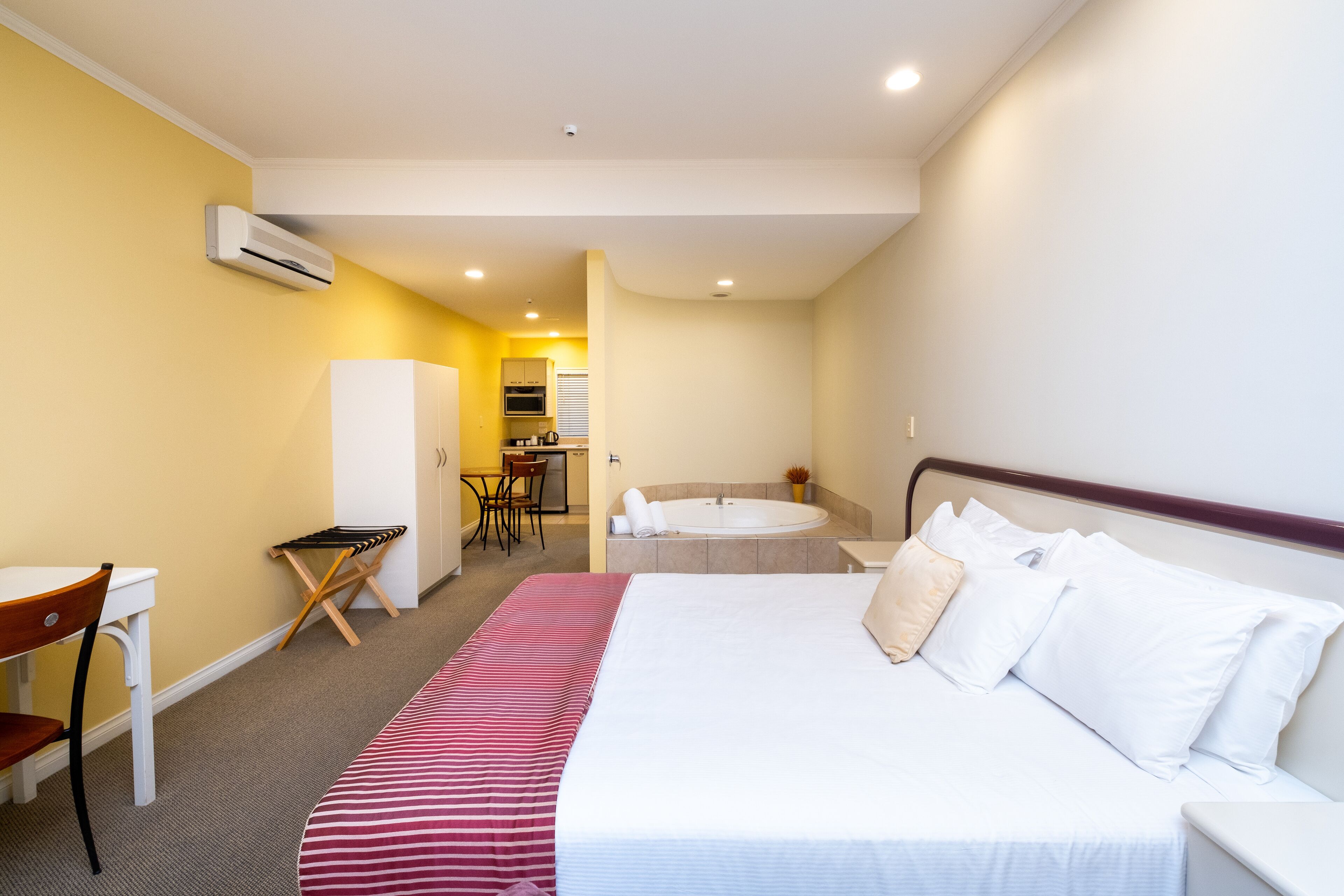 Una habitación de hotel con cama, escritorio, silla, kitchenette y baño.