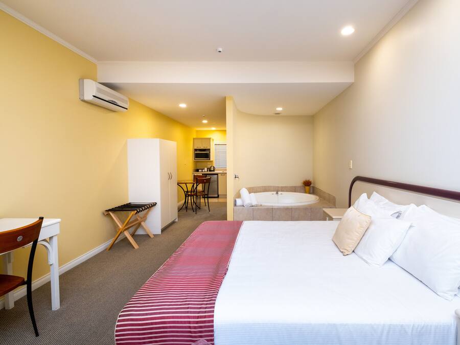 Una habitación de hotel con cama, escritorio, silla, kitchenette y baño.