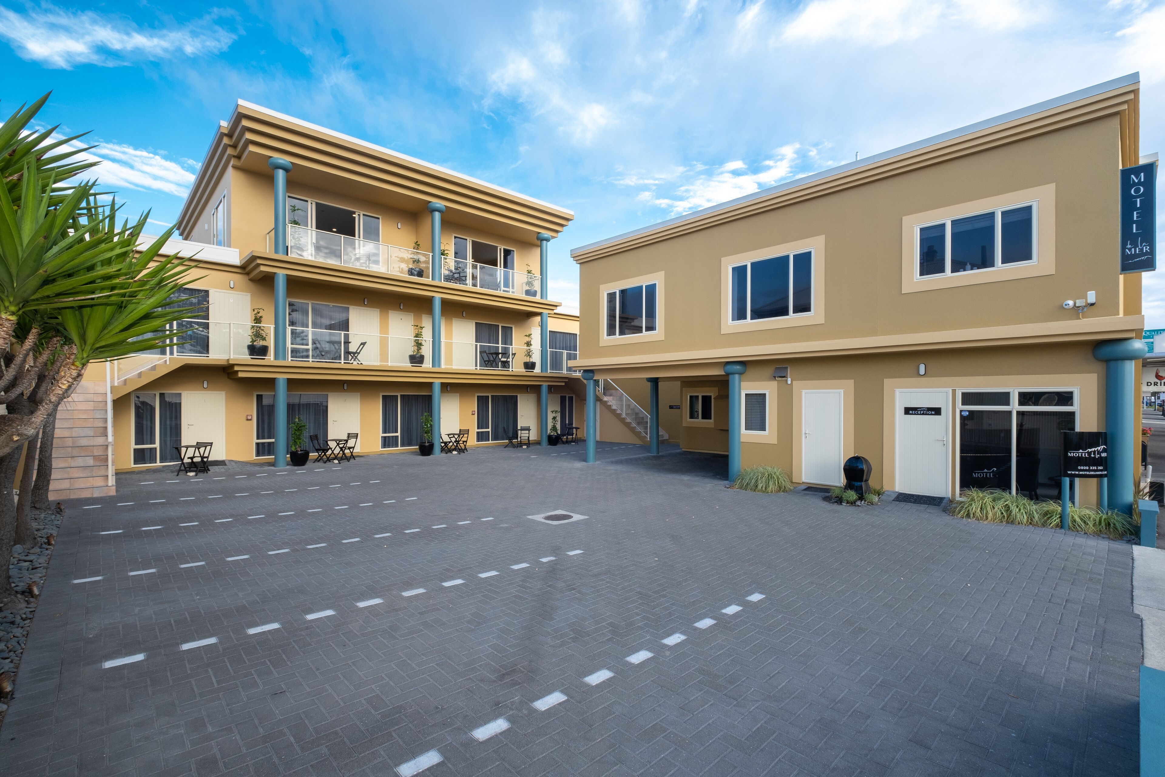 A two-story motel with a flat roof, a covered outdoor seating area, and a clear sky.
