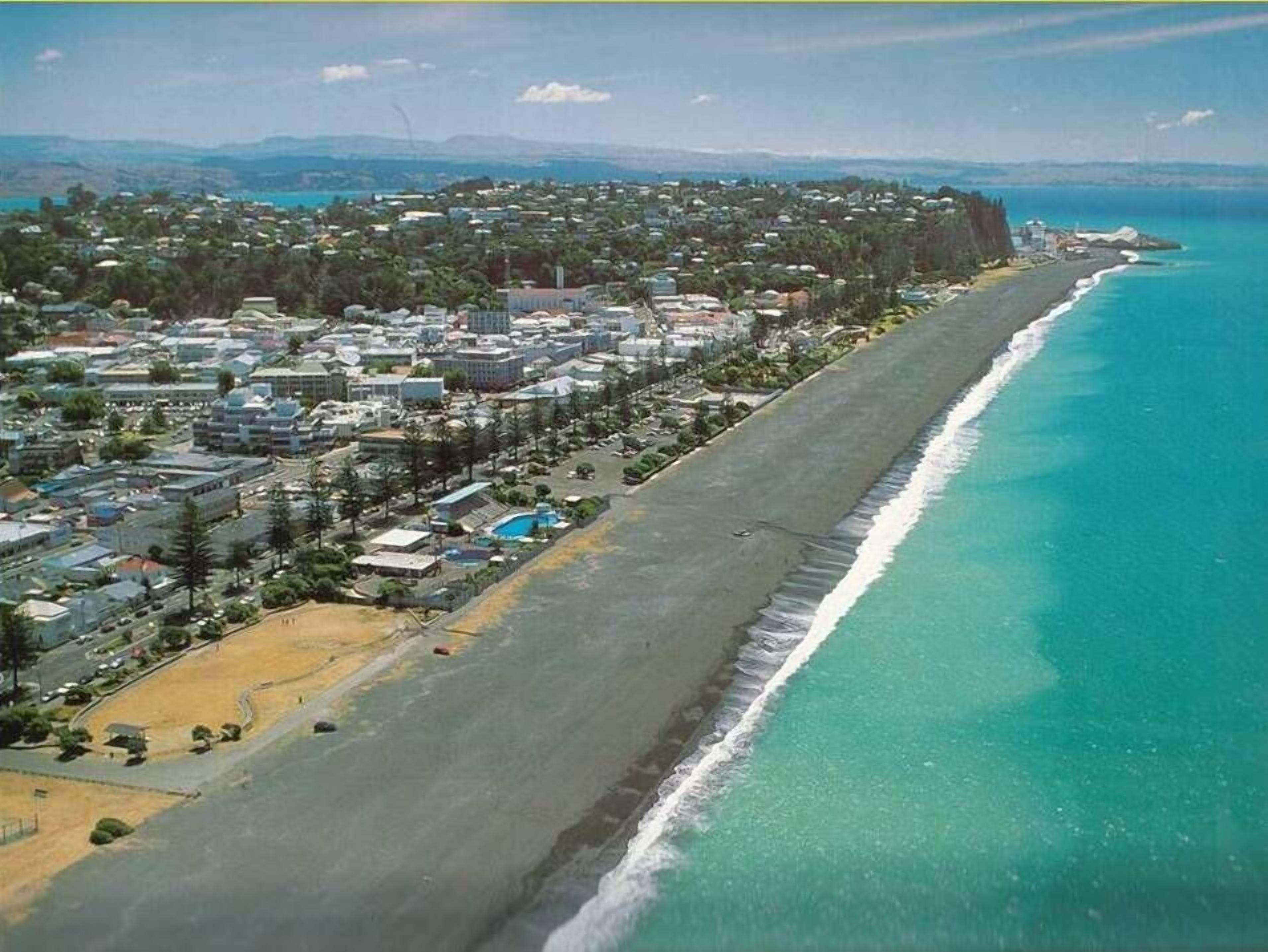 Vista aérea de una ciudad costera con una extensa playa, una zona urbana densa y un faro destacado.