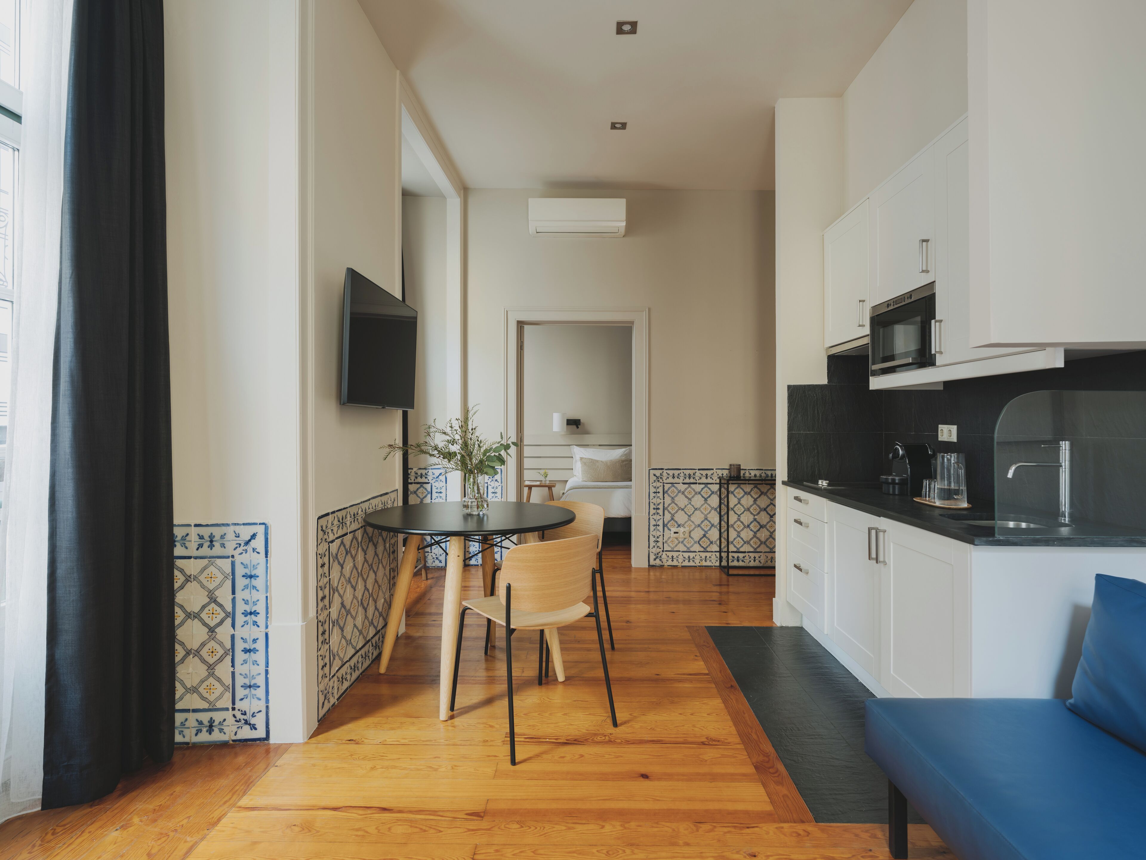 A modern kitchen with white cabinets, a black countertop, and a built-in microwave. There is a dining area with a table and chairs, and a blue sofa in the corner.