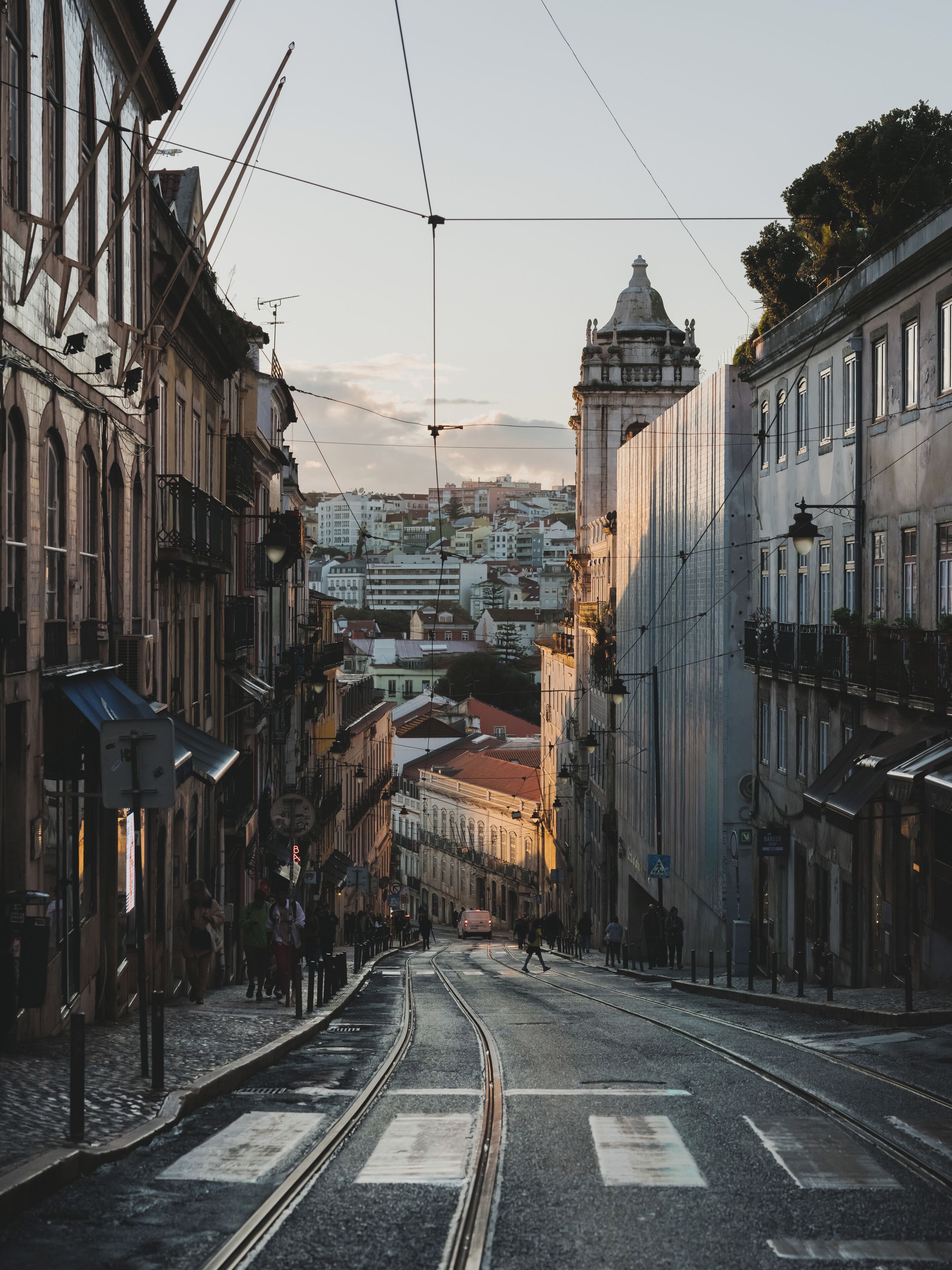 A street with tram tracks, buildings on either side, and a distant view of a cityscape.