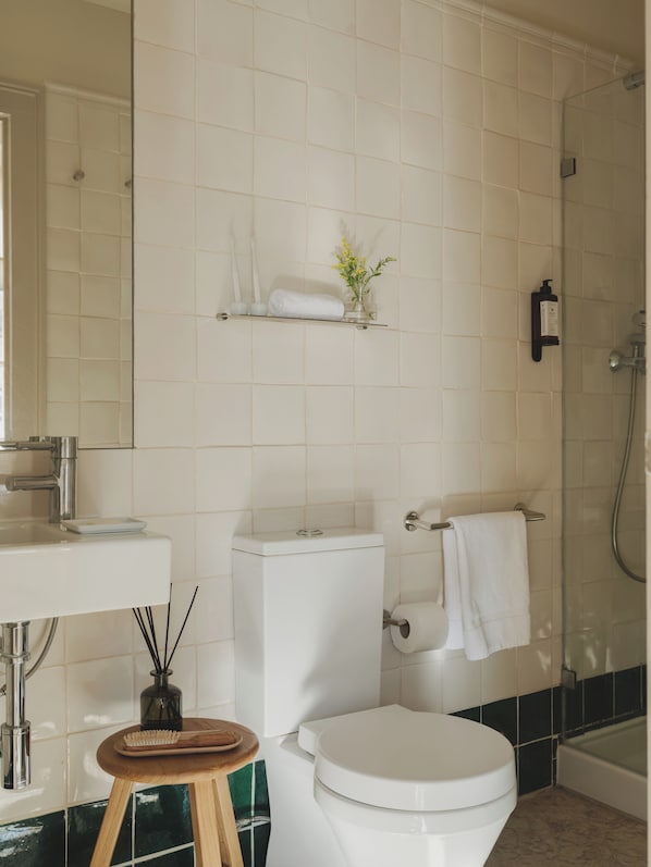 Une salle de bain équipée de toilettes, d’un lavabo et d’une douche. On y trouve des étagères avec des articles de toilette et une petite plante.