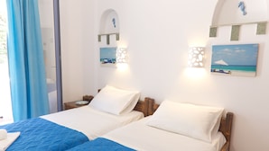 A hotel room with two beds, a large window with blue curtains, and wall-mounted artwork depicting a beach scene. - Aquarius Village Agistri (Agistri)