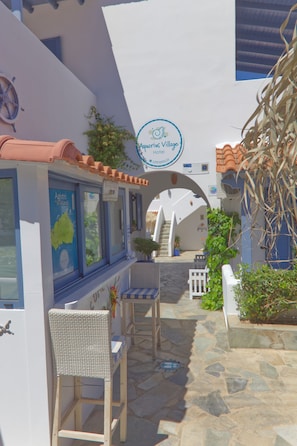 A narrow courtyard with a white building, a blue sign, and a wooden chair. - Aquarius Village Agistri (Agistri)