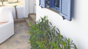 A white building with blue shutters, a stone-paved patio, and a view of olive trees. - Aquarius Village Agistri (Agistri)
