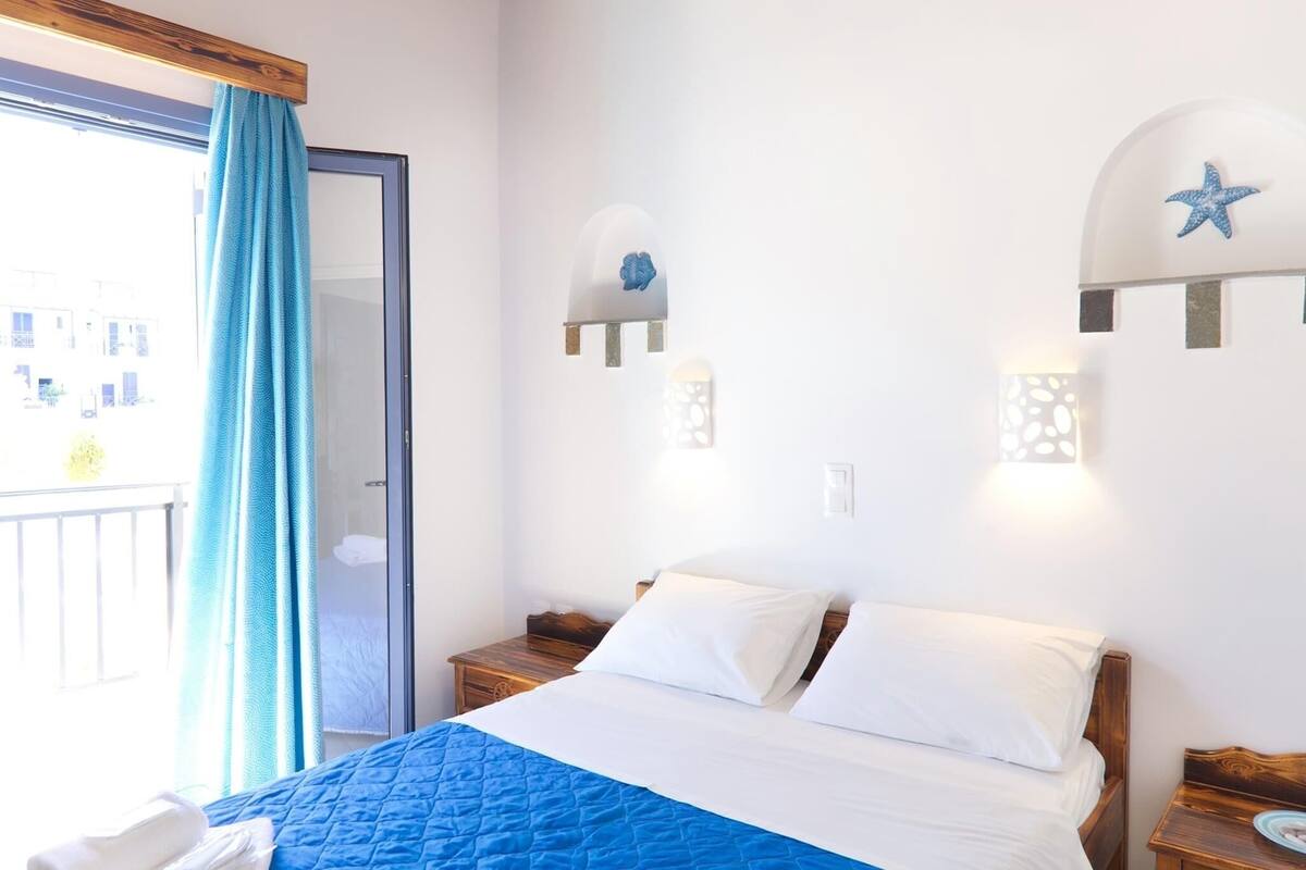 A bedroom with a bed, a wooden nightstand, a window with a blue curtain, and wall-mounted lights with star decorations.