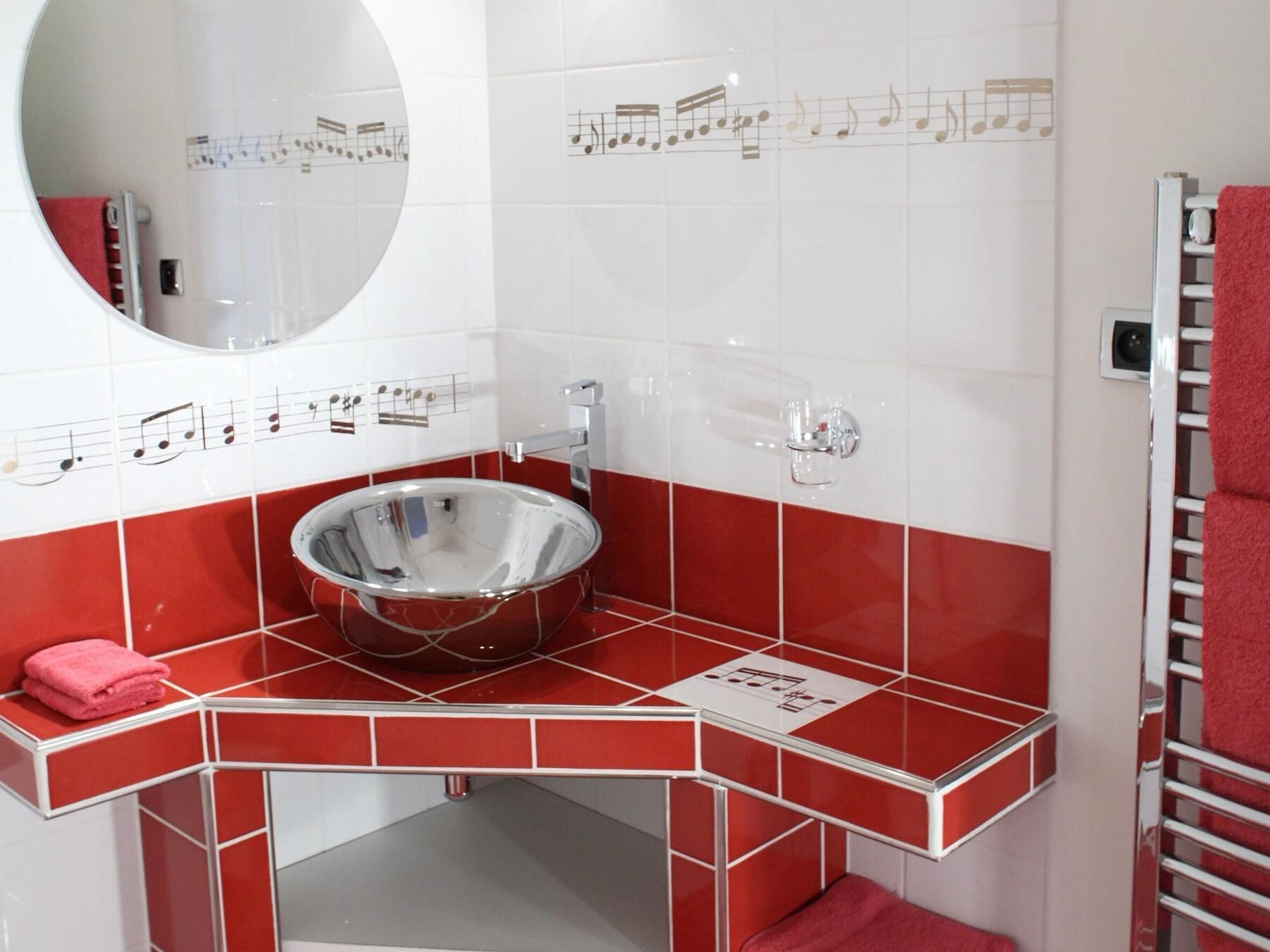 A bathroom with a round sink, red and white tiles, a mirror, and a towel rack.