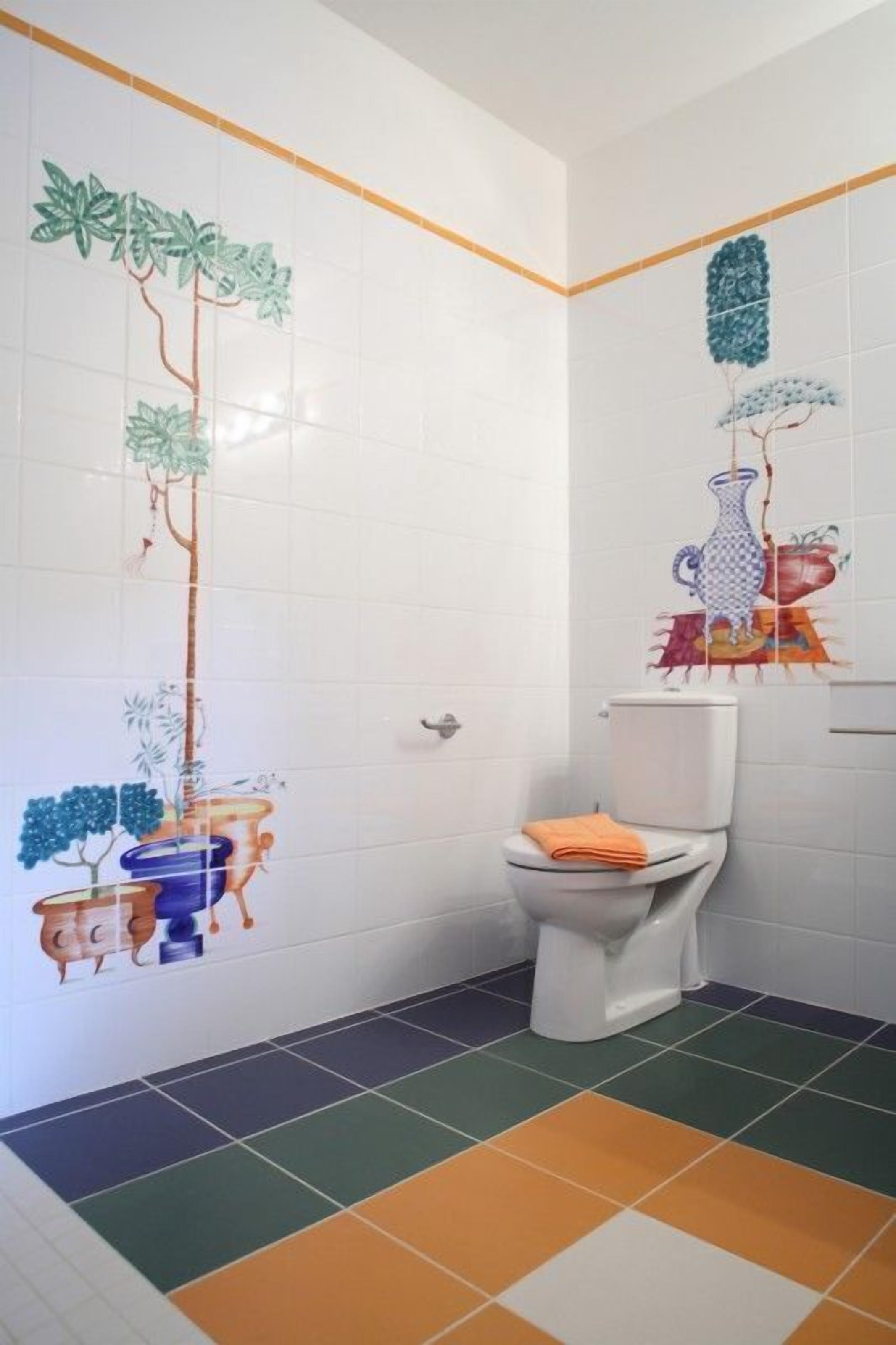Een badkamer met witte betegelde wanden, een toilet en kleurrijke vloertegels.