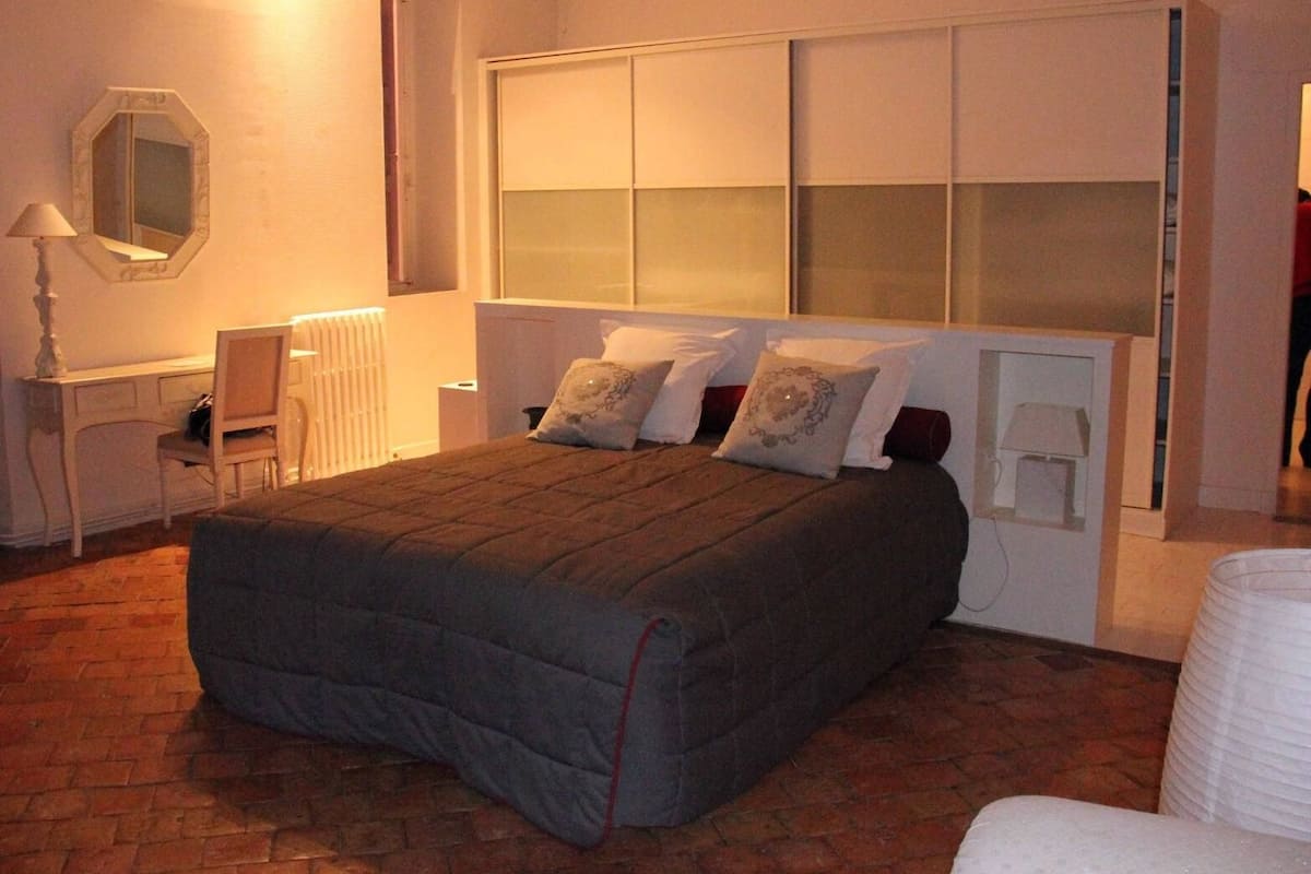 A bedroom with a large bed, a desk, a chair, a mirror, and a radiator.