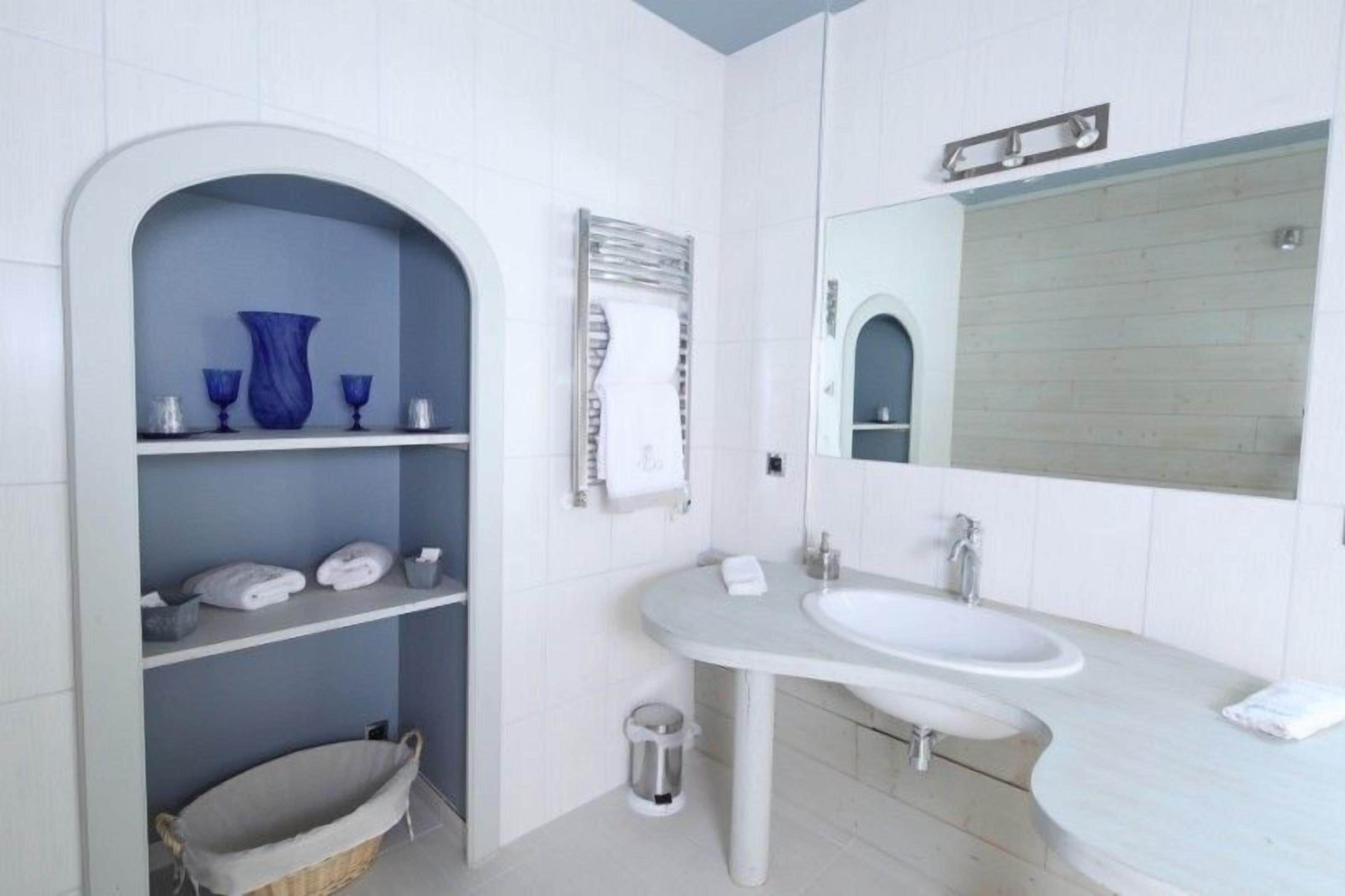 Een moderne badkamer met een wit wastafelmeubel, een grote spiegel en een blauwe vaas op een plank.