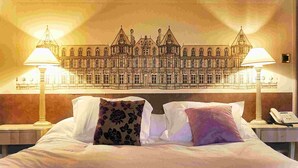 A hotel room with a large bed, two bedside lamps, and a wall mural of a historic building. - Le Relais Louis XI (Meung-sur-Loire)