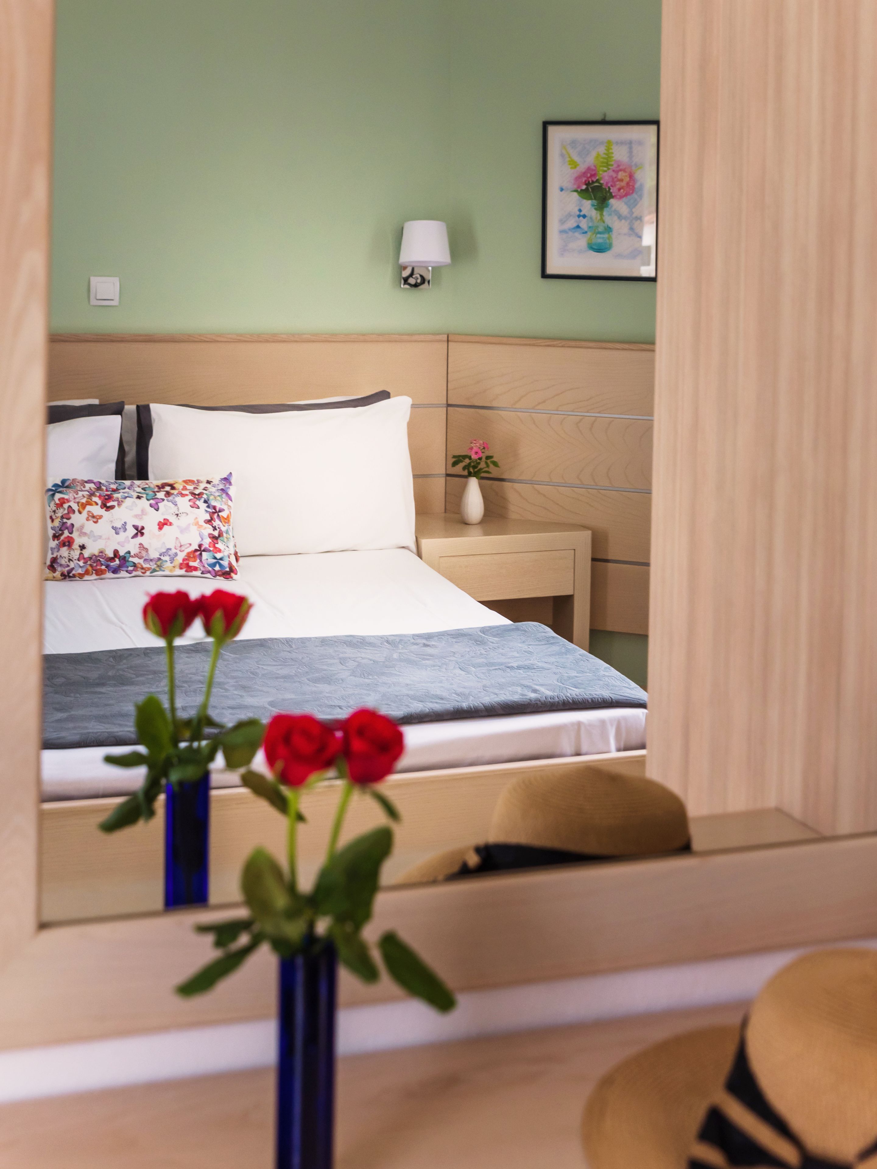 A bedroom with a bed, bedside table, lamp, and a mirror reflecting the room.