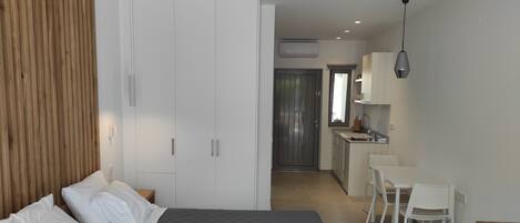 Une chambre moderne avec un grand lit, un mur recouvert de panneaux en bois, une armoire blanche et un coin cuisine comprenant une table et des chaises.