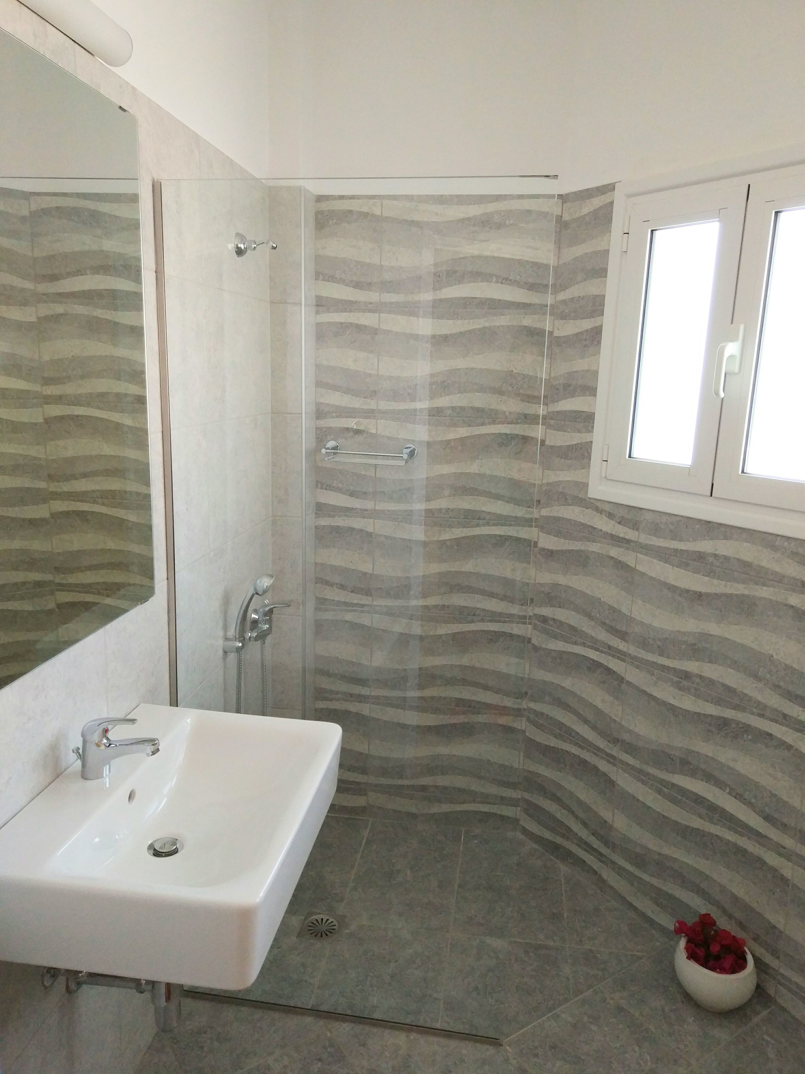 A bathroom with a white sink, a glass shower enclosure, and a patterned wall.