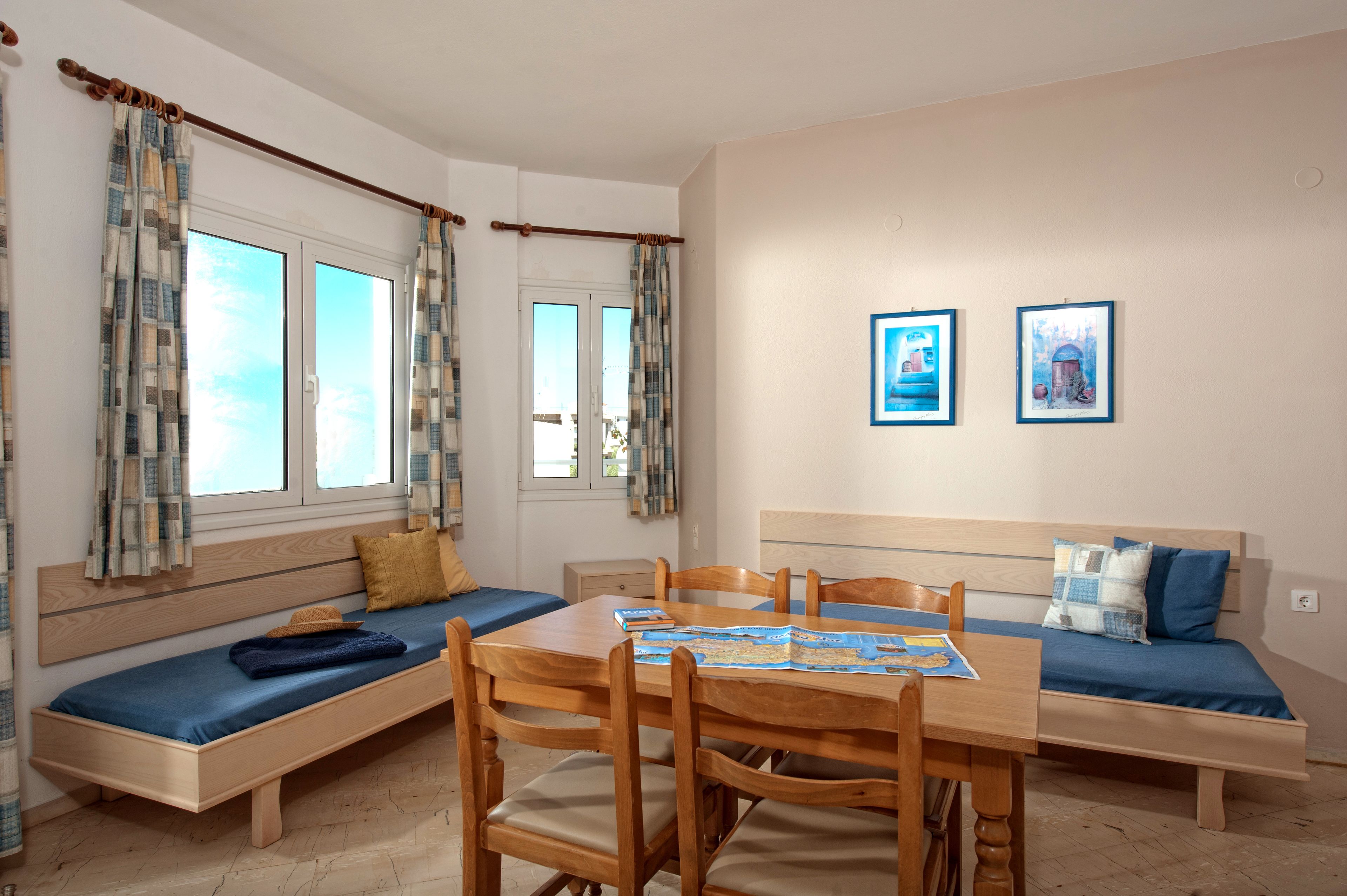 A room with a wooden dining table, two wooden benches, a sofa, and a window with curtains.
