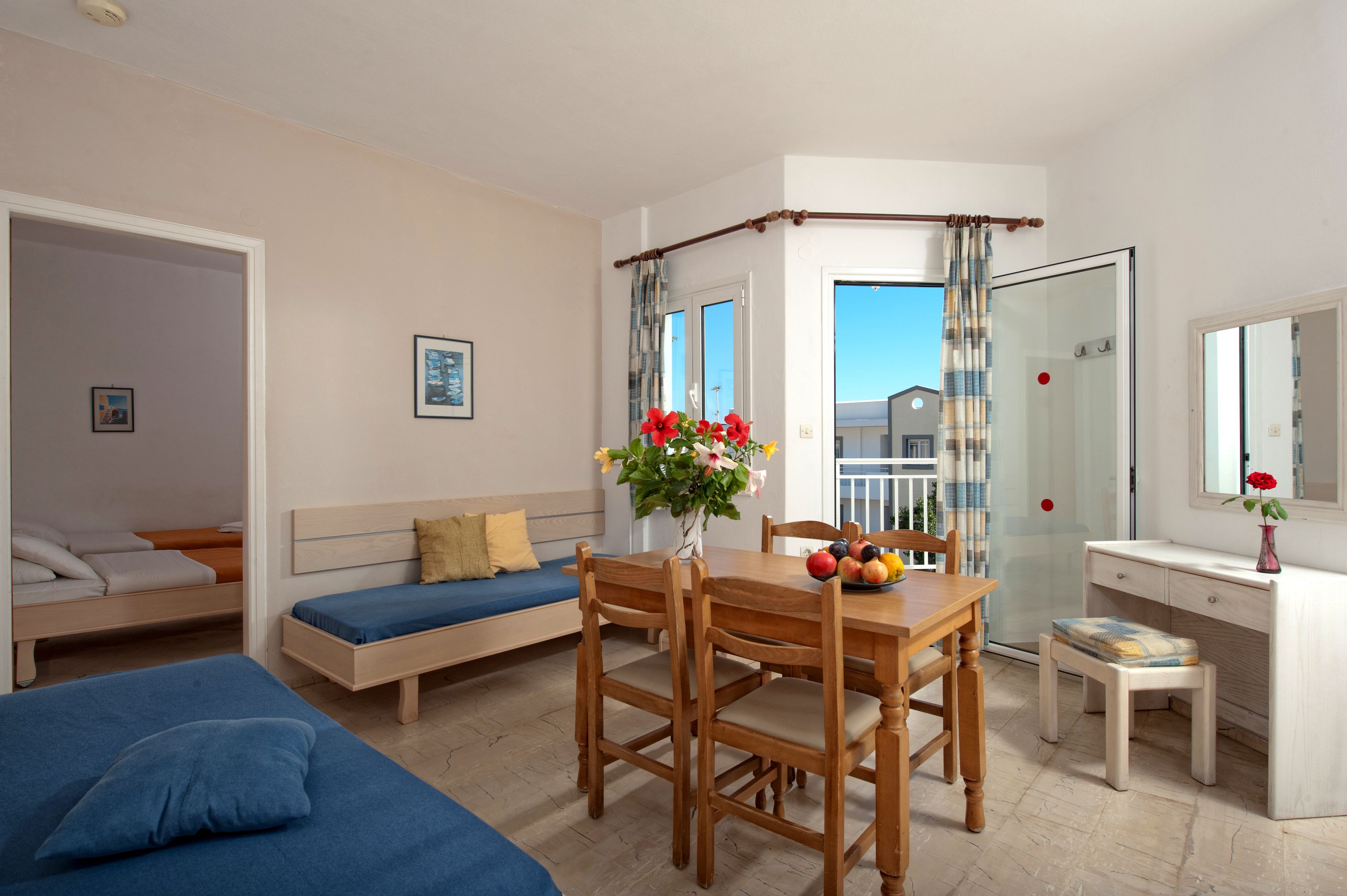 A room with a bed, a sofa, a dining table with chairs, a small desk, and a shower area.