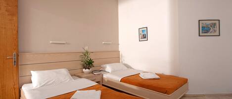 A hotel room with two beds, a wooden door, a nightstand with a plant, and two framed pictures on the wall.