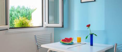 A dining area with a table, two chairs, a plate with watermelon, a glass of orange juice, and a vase with a rose.