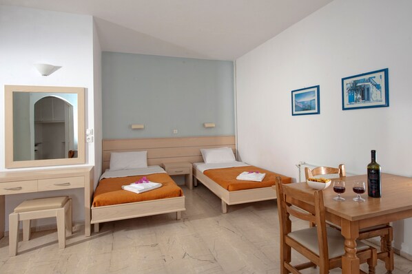 A hotel room with two beds, a desk with a chair, a small stool, a table with two glasses and a bottle, and two framed pictures on the wall. - Melissa Apartments, Studios & Suites (Hersonissos)