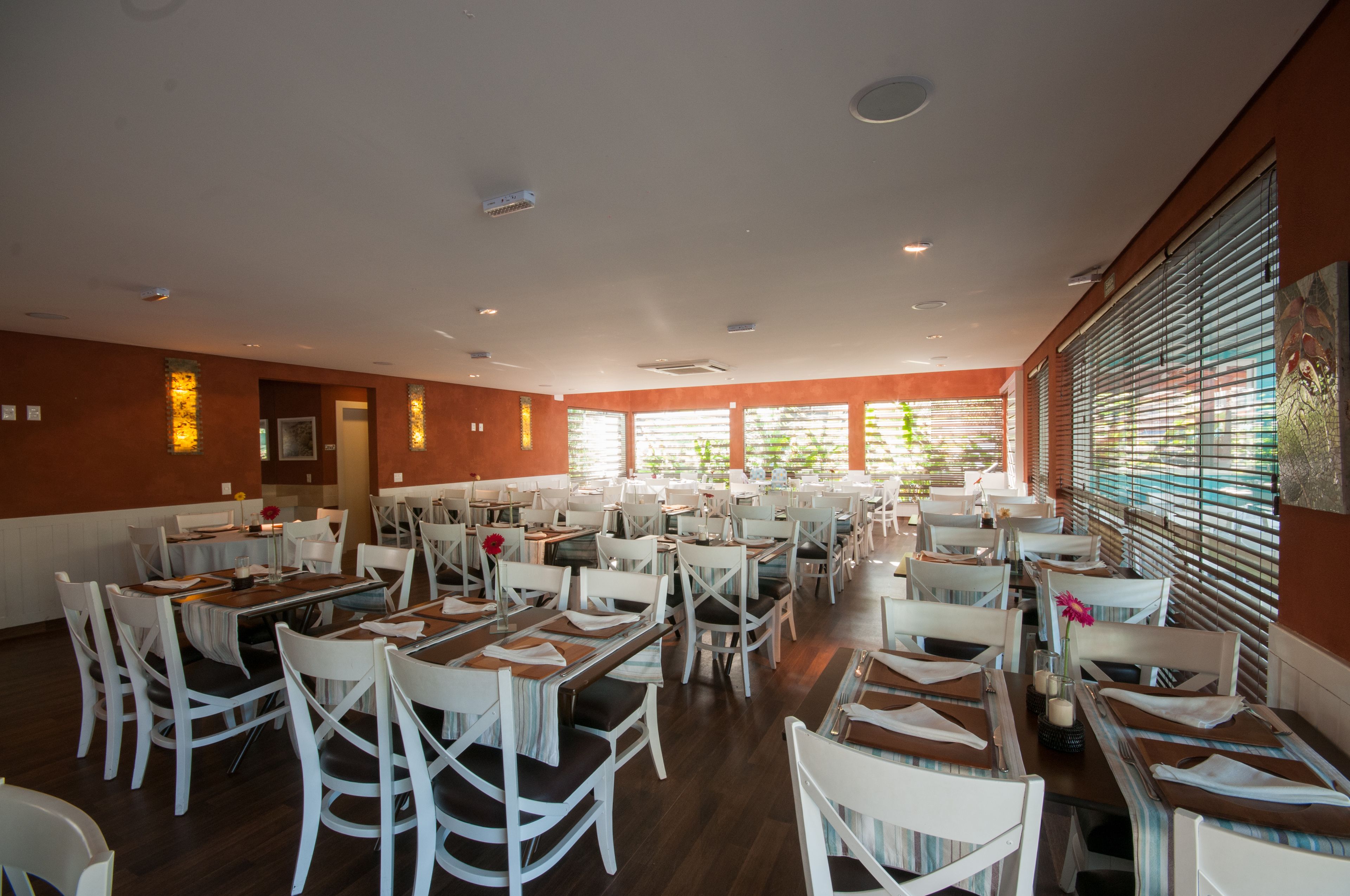 Un comedor espacioso con varias mesas y sillas, ventanas amplias con persianas y un diseño moderno de techo.