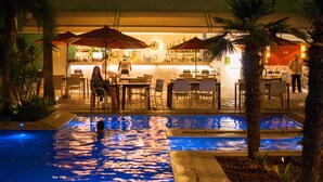 Een zwembadgedeelte met een bar en zitplaatsen, omringd door palmbomen en parasols.