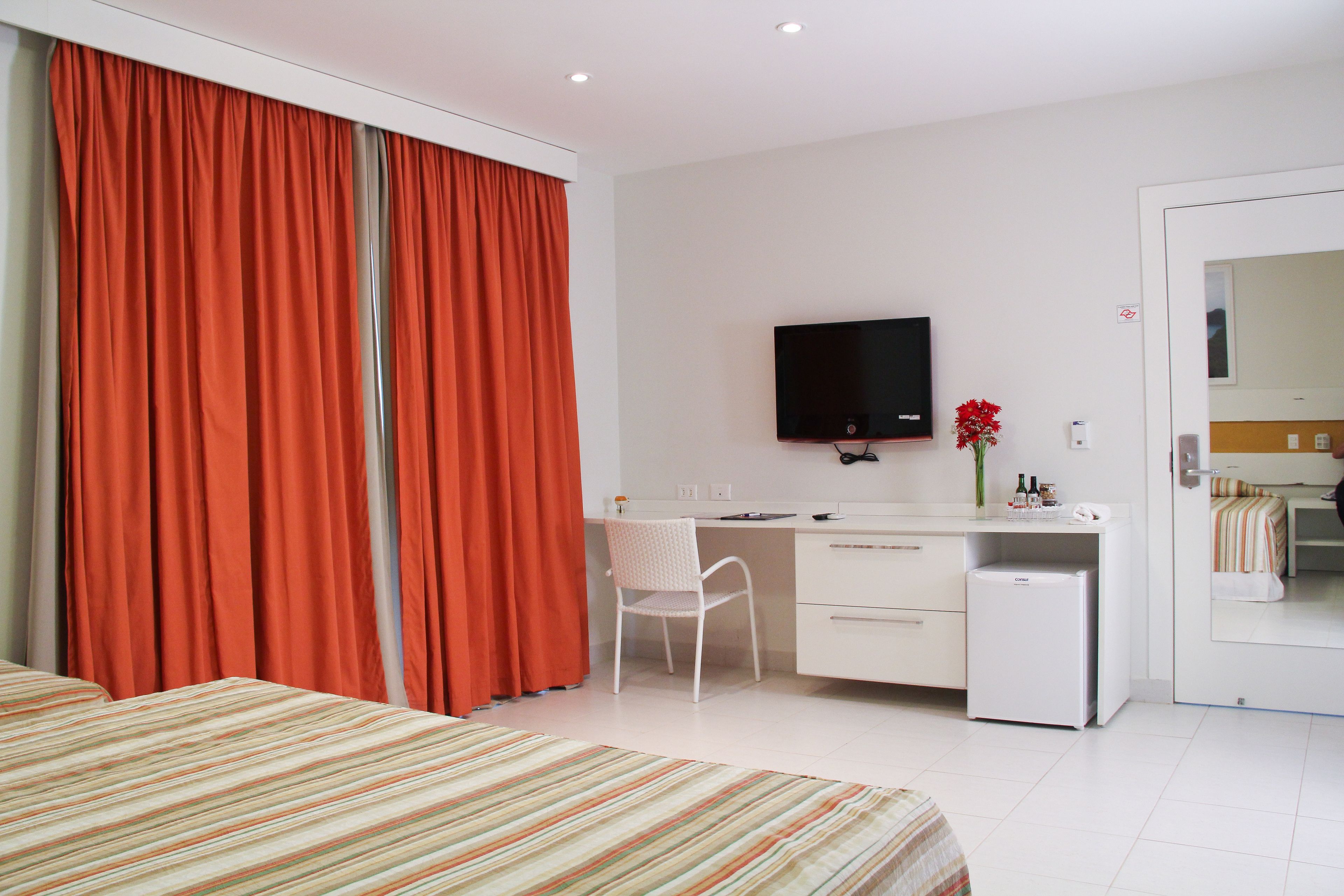 Une chambre d’hôtel équipée d’un lit, d’un bureau avec un ordinateur, d’une télévision et d’un petit réfrigérateur.