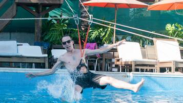 Un hombre en una piscina con una plataforma de madera y sillones de descanso al fondo.