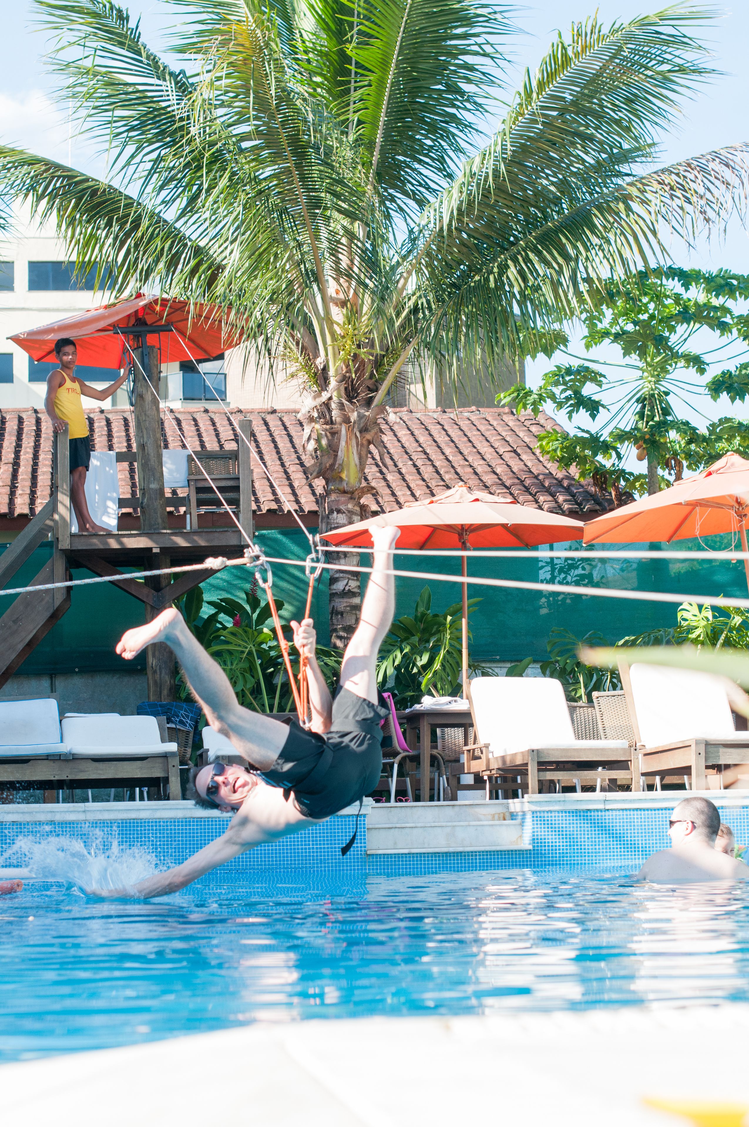 A swimming pool with a person diving into the water, surrounded by palm trees and umbrellas.