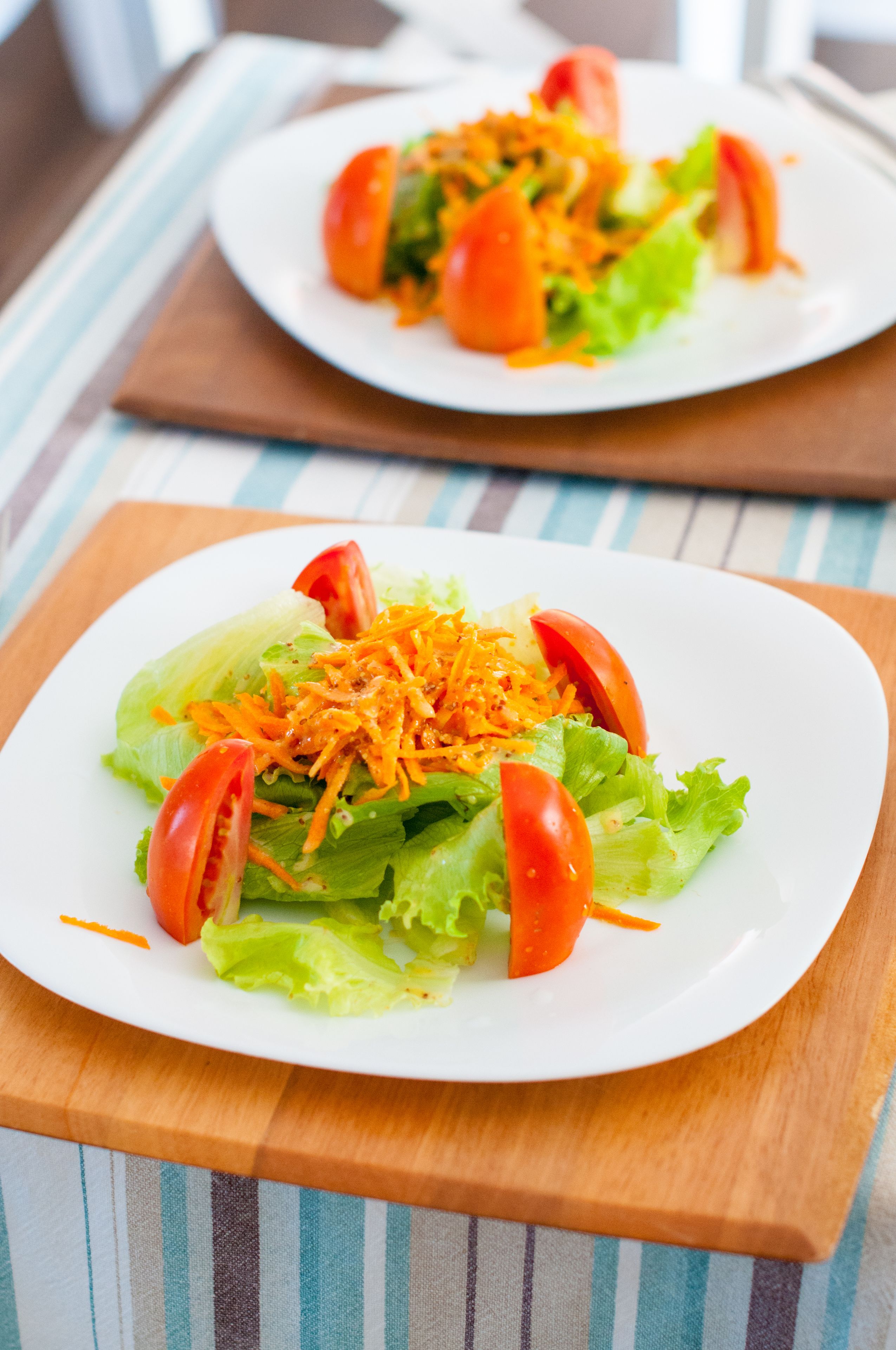 Uma salada com alface, tomates e queijo ralado sobre uma mesa de madeira.